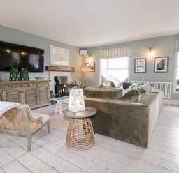 A living room with an olive green sofa a wicker side table and a large TV on a wooden cabinet at Louvain in Cadgwith near Ruan Minor