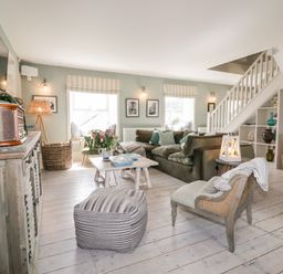 A living room with a sofa armchair ottoman coffee table and stairs at Louvain in Cadgwith near Ruan Minor