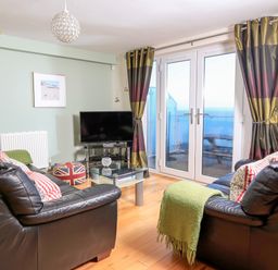 A living room with two black leather sofas a glass coffee table a television and double glass doors with striped curtains at 2 The Bay in Bigbury