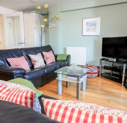 A living room with black leather sofas pillows a glass coffee table tv on stand and a floor lamp at 2 The Bay in Bigbury