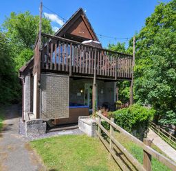A two story house with a balcony and a wooden fence surrounded by trees at 59 Valley Lodge in Callington near Gunnislake