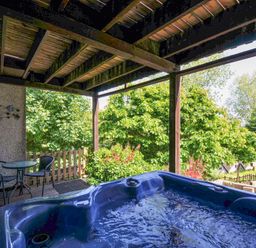 A covered outdoor deck with a hot tub and a small table with two chairs surrounded by trees at 59 Valley Lodge in Callington near Gunnislake