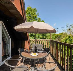 A wooden balcony with a round table and four chairs under a large umbrella at 59 Valley Lodge in Callington near Gunnislake