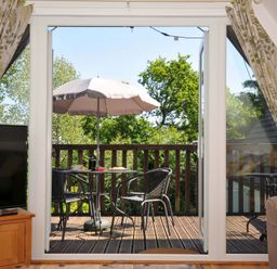 A balcony with a table umbrella and two chairs viewed from a room with a television and curtains at 59 Valley Lodge Callington near Gunnislake