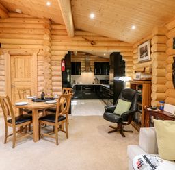 A wooden dining table with four chairs set with plates and glasses near a log cabin style kitchen with black cabinets and a black armchair in a living area at Jalan End in Felton