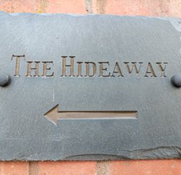 A stone sign with THE HIDEAWAY and an arrow pointing left on a brick wall at The Hideaway in Malvern