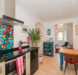A kitchen with a colorful stained glass backsplash a wooden dining table with chairs and a blue cabinet at The Hideaway in Malvern