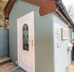 Exterior corner of a small building with a white door featuring decorative glass at The Nook Star near Cenarth