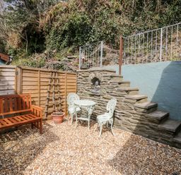 An outdoor patio area with wooden bench metal table and chairs stone steps and a statue at The Nook Star near Cenarth