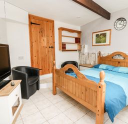 A bedroom with a wooden bed blue bedding a black chair a wooden door a wall clock and a television at The Nook Star near Cenarth