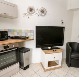 A kitchen corner with an oven microwave trash can television on a small table and a black chair at The Nook in Star near Cenarth