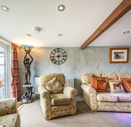 A living room with patterned armchairs and sofa a statue lamp a clock and a framed photo at Pendre Cottage in Cenarth