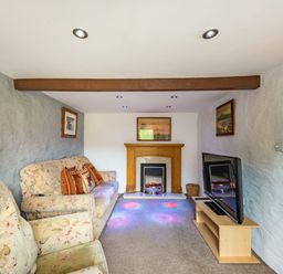 A living room with floral sofas a fireplace a television on a stand and framed pictures on the walls at Pendre Cottage in Cenarth