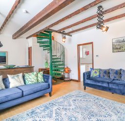 A living room with two blue sofas with cushions a blue patterned rug wooden beams on the ceiling a green spiral staircase and a doorway at The Brewery Brewers Quay Harbour