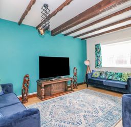 A living room with blue sofas a large patterned rug a wooden tv stand a flat screen tv and wooden ceiling beams at The Brewery in Brewers Quay Harbour