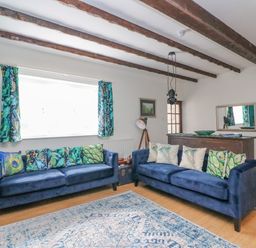 A living room with two blue sofas and patterned cushions with exposed wooden beams on the ceiling at The Brewery in Brewers Quay Harbour