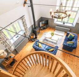 A living room with blue sofas pillows a wood stove a coffee table and a spiral staircase at Greystead Institute in Bellingham