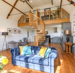 A living room with blue sofas yellow and blue cushions wooden spiral staircase and kitchen at Greystead Institute in Bellingham