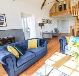 A living room with blue sofas yellow and blue cushions wooden spiral staircase and flowers on a table at Greystead Institute in Bellingham