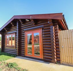 An exterior view of a small log cabin with wooden double doors and a window next to a wooden fence at Rowan Lodge in Greetham Rutland