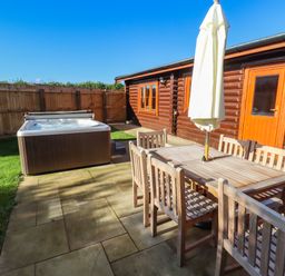 An outdoor patio area with wooden dining table and chairs a hot tub and a wooden cabin at Rowan Lodge in Greetham Rutland