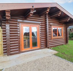 A wooden log cabin with glass double doors and a window on a grassy area at Maple Lodge in Greetham Rutland