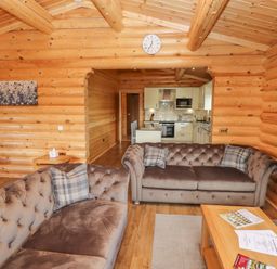 A living room with two brown sofas and a wooden coffee table opening to a kitchen at Maple Lodge in Greetham Rutland