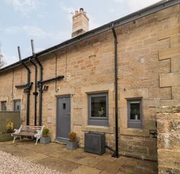 Stone exterior of a cottage with gray doors and windows and a bench at Grange Cottages in Alnwick