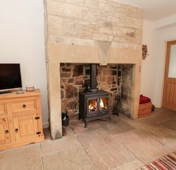 A stone fireplace with a wood-burning stove next to a wooden cabinet with a television at Grange Cottages in Alnwick