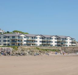 A sandy beach with people and umbrellas in front of apartment buildings at 17 Burgh Island Causeway in Bigbury-On-Sea