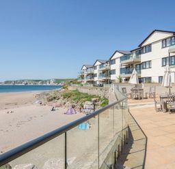 A beach with sand and people near a row of white buildings with balconies and patio tables at 17 Burgh Island Causeway in Bigbury-On-Sea