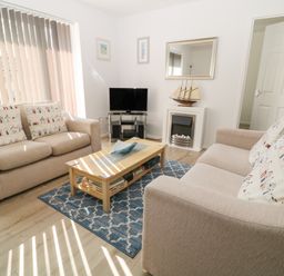 A living room with two beige sofas cushions with house patterns coffee table a TV on stand a wall mirror and a model ship at Ballasalla in Liskeard