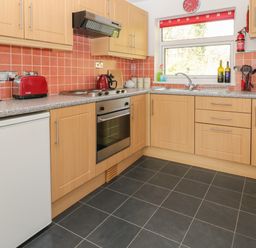 A kitchen with wooden cabinets red toaster and kettle and utensils on countertop at Ballasalla in Liskeard