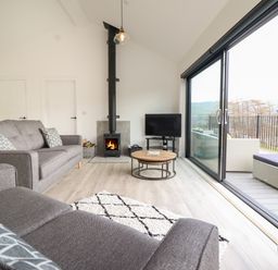 A living room with gray sofas a wood stove and a sliding door leading to a balcony at The Sheep Shed in Llanrhaeadr-Ym-Mochnant
