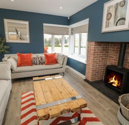 A living room with two sofas orange cushions a wooden coffee table a fireplace and a wicker basket for firewood at The Deck House in Beadnell