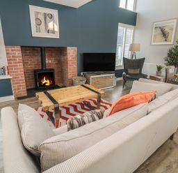 A living room with a wood stove fireplace a striped sofa a wooden coffee table and a television at The Deck House in Beadnell