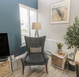 A corner of a living room with a gray armchair and a television on a wooden trunk at The Deck House in Beadnell