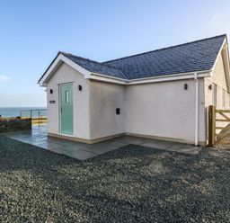 A single story house with a blue door and gravel driveway near the sea at Y Gorlan in Moelfre
