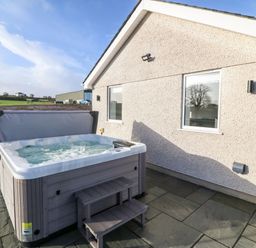 An outdoor hot tub with water and steps beside a house with two windows and stone tiles at Y Gorlan in Moelfre