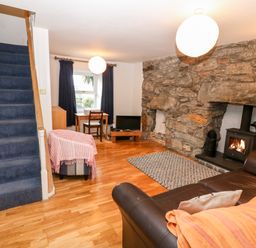 A living room with a stone fireplace a wood stove a brown leather sofa a blue carpeted stairway and a small wooden desk at Gerlan in Harlech