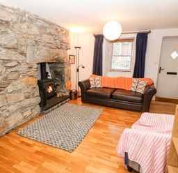 A living room with a stone fireplace a wood stove a brown sofa with cushions a patterned rug and a pink striped chair at Gerlan in Harlech