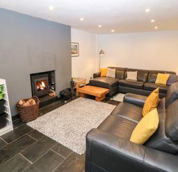 A living room with a black leather sofa set a wooden coffee table a fireplace with fire a gray wall and storage bins at Gerlan in Harlech