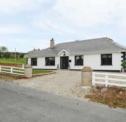 A single story white house with grey roof and black windows with gravel driveway and white fence at Gatehouse in Moville County Donegal