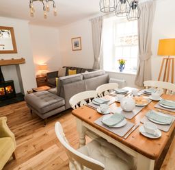 A dining table set with cups plates and a teapot next to a living room with a fireplace sofa and armchair at Curlew Cottage 2 Fenkle Street Holy Island