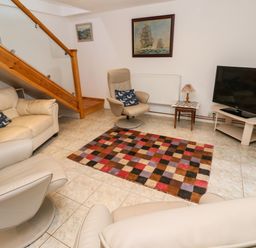 A sitting room with beige armchairs a sofa a multicolored checkered rug a television on a stand and a wooden staircase at Alice Cottage in Wheal Kitty near St Agnes