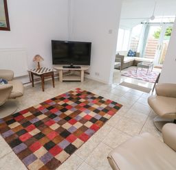 A living room with two beige chairs a multicolored checkered rug a small table with a lamp and a television at Alice Cottage in Wheal Kitty near St Agnes