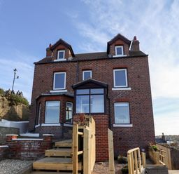 A brick house with multiple windows and wooden stairs leading up to the entrance at Mariners Watch in Whitby