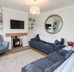 A living room with two blue sofas a blue armchair a fireplace with fire a wall-mounted TV and shelves with decorations at Mariners Watch in Whitby