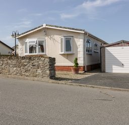 A single-story house with bay windows a stone wall and a garage with a white door at Summer Breeze in Tregolds near St Merryn