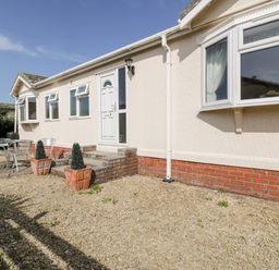 A gravel front yard with steps leading to a white door and metal patio furniture at Summer Breeze in Tregolds near St Merryn